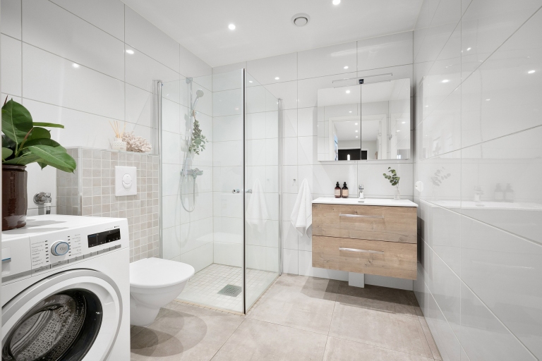 White bathroom with a stacked washer, walk-in shower and floating vanity